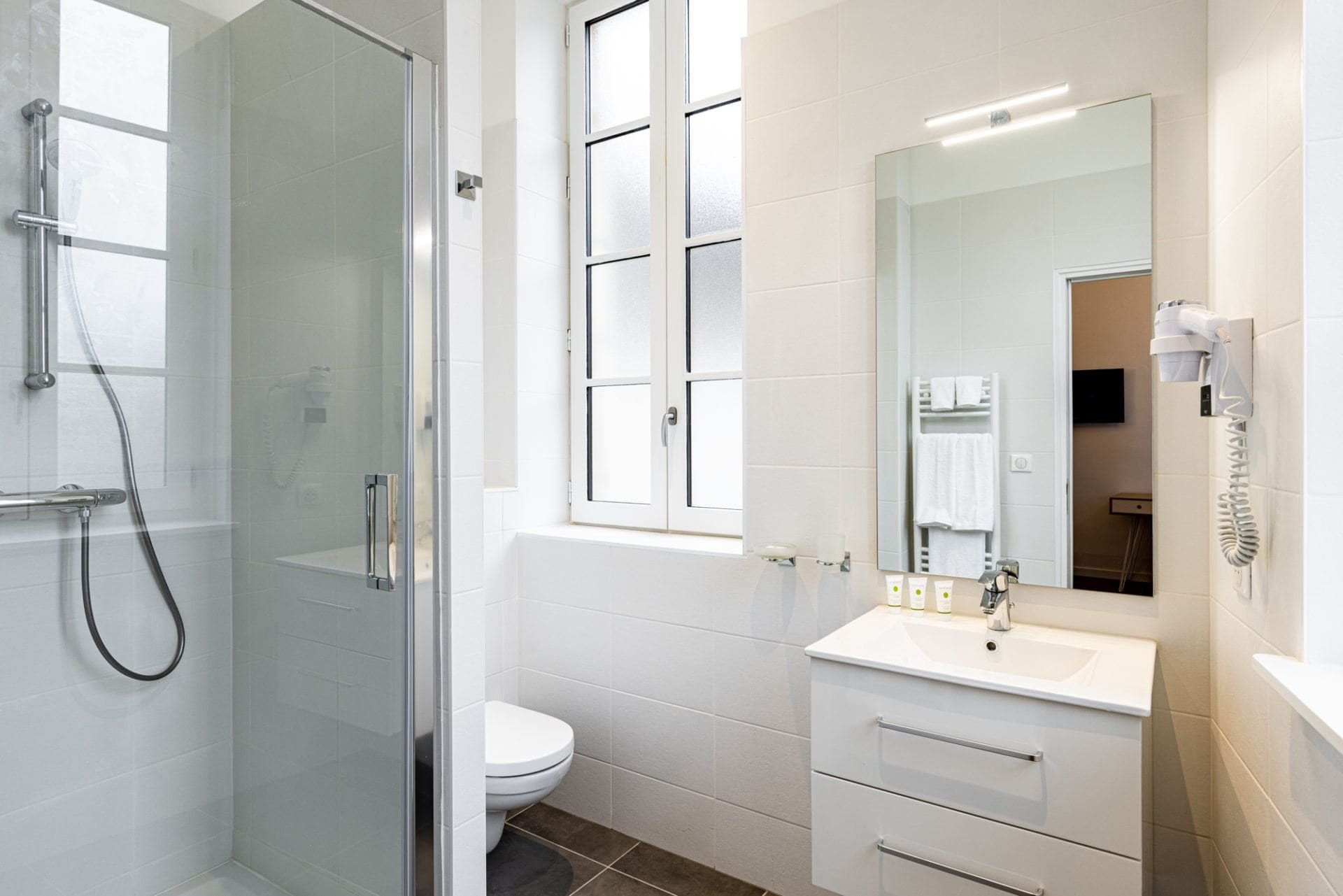 Salle de bain lumineuse équipée d'un sèche serviette et d'un sèche cheveux. Cabine de douche et WC